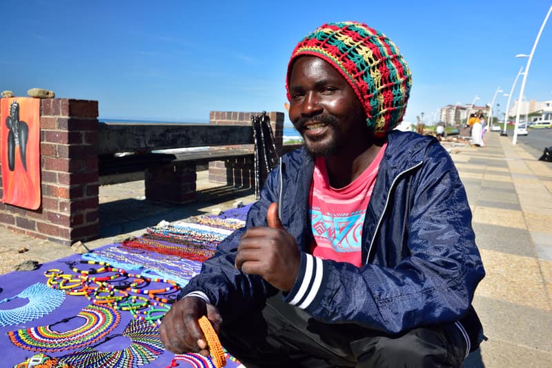 A beadwork trader on the East London beachfront giving a thumbs-up beside his spread of beaded jewellery.