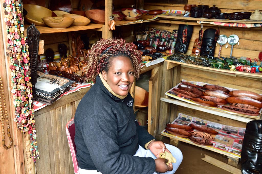 A craft-shop owner in Graskop, Mpumalanga, seated at her counter among shelves of carved wooden bowls and beadwork.