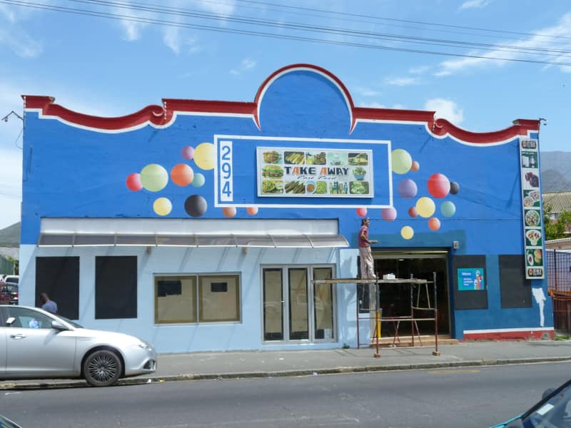 A bright blue takeaway shopfront with painted circles on a street in Woodstock, Cape Town.